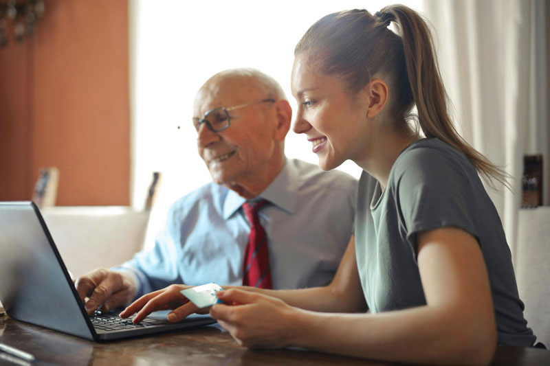 Elderly man and young woman using a laptop, smiling as they work together.