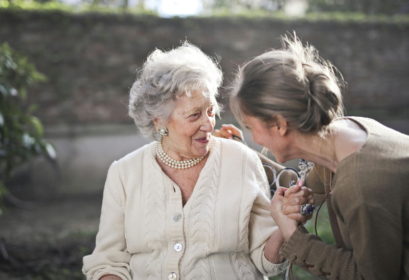 Elderly woman smiling while holding hands with a younger woman.